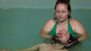 Adam yüzme havuzunda kafa masajı yapıyor.