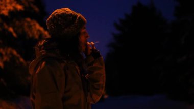 Kışın, kışın gece dışarıda sigara içen adam.