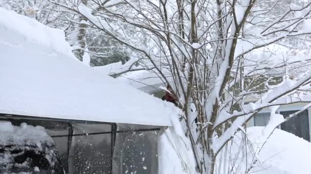 Man verwijdert sneeuw uit het bladerdak boven auto in een winter scene — Stockvideo