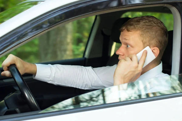 Młody człowiek rozmawia przez telefon, za kierownicą samochodu — Zdjęcie stockowe