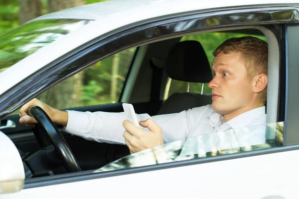 Jovem usa o telefone ao volante de um carro — Fotografia de Stock