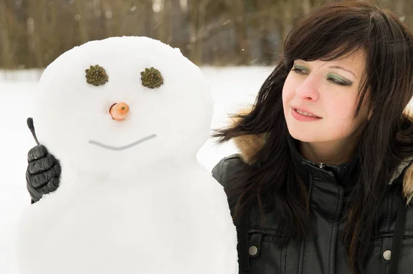 Vacker flicka vilar på den natur som kramar en snögubbe — Stockfoto