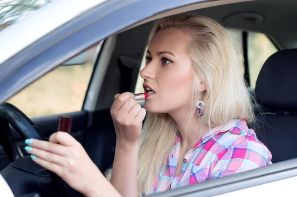 Girl paints her lips at the wheel the car Stock Picture