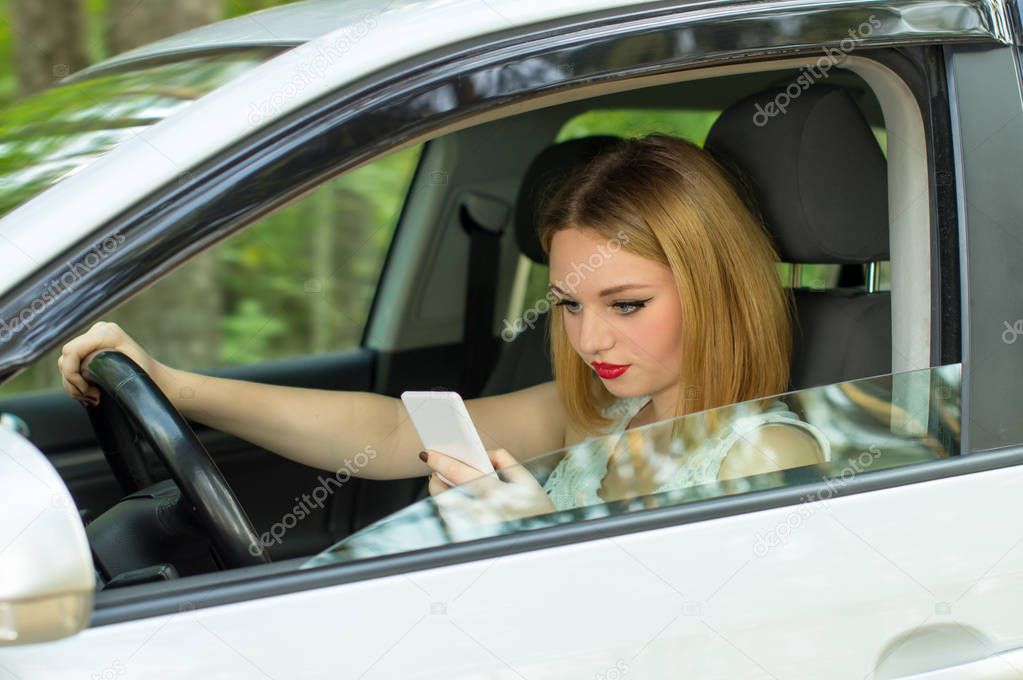Beautiful girl behind the wheel of a car, looking phone