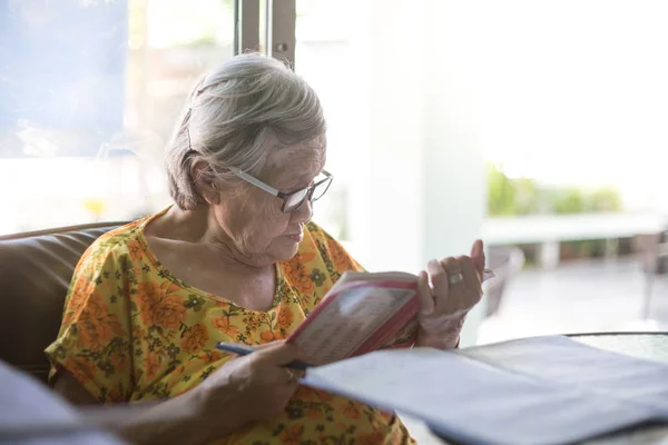 Asian old woman Sitting and writing on the table by the glass wi