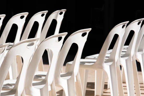 Fila de sillas de plástico blanco en el sol sobre un fondo negro.sha —  Fotos de Stock