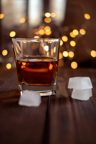 A glass of whiskey or rum with ice on a dark and bokeh background — Stock Photo, Image