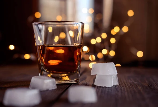 A glass of whiskey or rum with ice on a dark and bokeh background — Stock Photo, Image