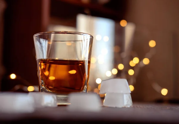 A glass of whiskey or rum with ice on a dark and bokeh background — Stock Photo, Image