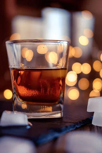 A glass of whiskey or rum with ice on a dark and bokeh background — Stock Photo, Image