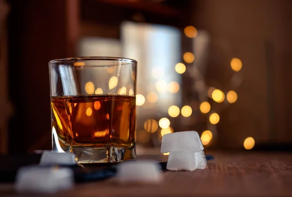 A glass of whiskey or rum with ice on a dark and bokeh background — Stock Photo, Image