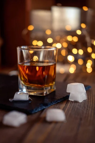 A glass of whiskey or rum with ice on a dark and bokeh background — Stock Photo, Image