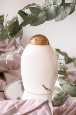 Bottles of cosmetics: body lotion, cream, or hair or body care products. Light background with eucalyptus leaves.