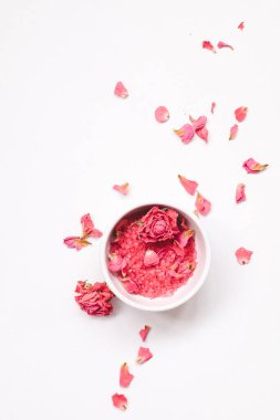 Deniz tuzu ve özlü beyaz kase ve gül kokusu, açık arkaplanda kurumuş gül tomurcukları.