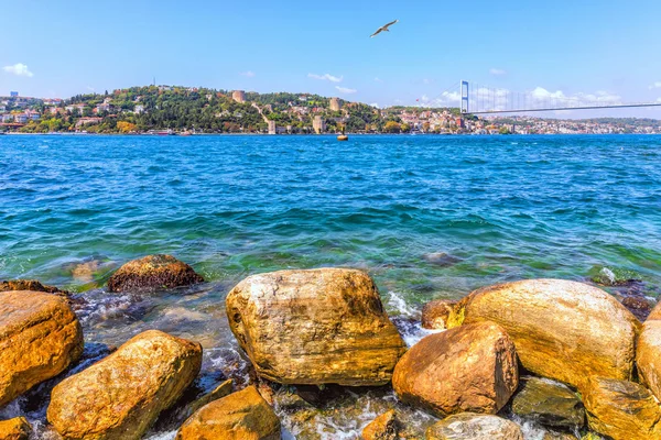 Bosphorus pobřeží kameny, Sultan Fatih Mehmet most a Rumeli Hisari v pozadí — Stock fotografie