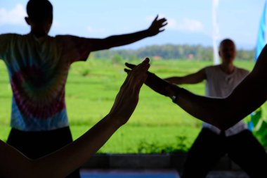 Gölgedeki insanların elleri arka planda bir yön öğretmeniyle qigong enerjisi alıştırması yapıyor.. 