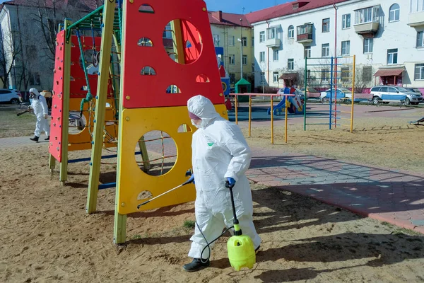 Koruyucu kıyafetli ve maskeli bir kadın çocuk parkını dezenfekte ediyor. COVID-19 enfeksiyonu ve kitle alımının yayılmasını önlemek için önlemler