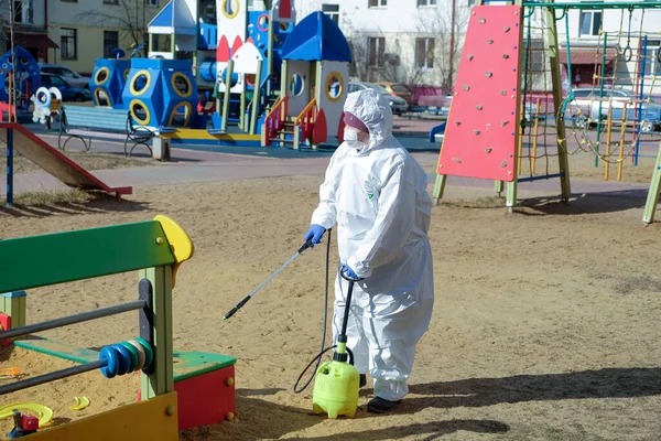 Koruyucu kıyafetli ve maskeli bir kadın çocuk parkını dezenfekte ediyor. COVID-19 enfeksiyonu ve kitle alımının yayılmasını önlemek için önlemler
