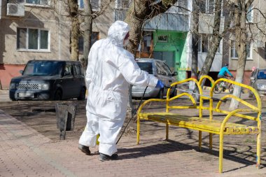 Koruyucu kıyafetli ve maskeli bir kadın çocuk parkını dezenfekte ediyor. COVID-19 enfeksiyonu ve kitle alımının yayılmasını önlemek için önlemler