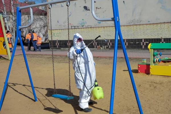 RAMENSKOYE, RUSSIA - 26 Mart 2020: Koruyucu giysili ve maskeli kadın çocuk oyun alanını dezenfekte ediyor. COVID-19 enfeksiyonu ve kitle alımının yayılmasını önlemek için önlemler