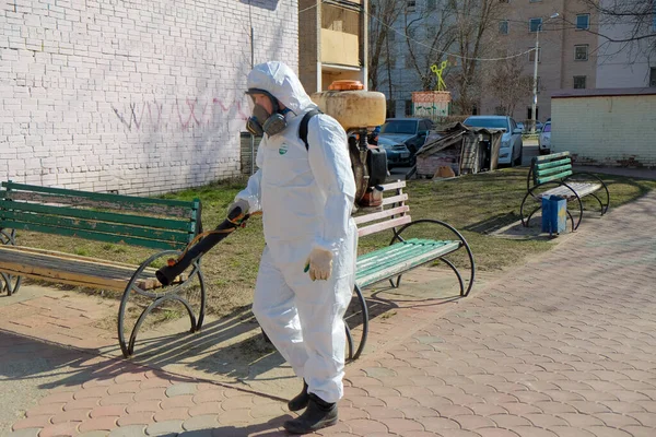 Koruyucu kıyafetli ve maskeli bir adam çocukların oyun alanını dezenfekte ediyor. COVID-19 enfeksiyonu ve kitle alımının yayılmasını önlemek için önlemler.