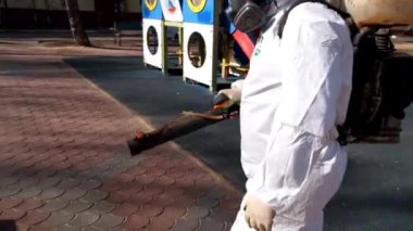 Koruyucu kıyafetli ve maskeli bir adam çocukların oyun alanını dezenfekte ediyor. COVID-19 enfeksiyonu ve kitle alımının yayılmasını önlemek için önlemler