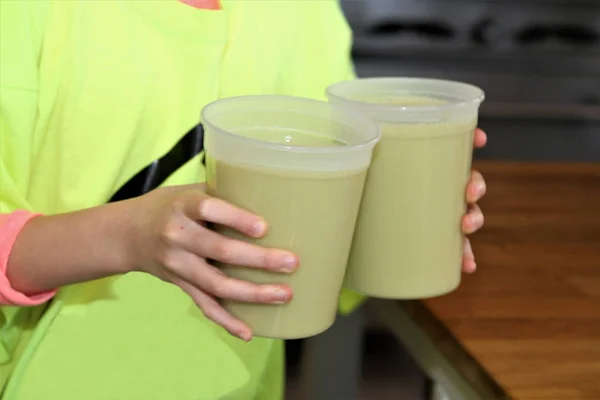 Hands holding puree asparagus soup in plastic containers