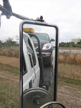 Reflections in mirror of a car on flatbed of towtruck clipart