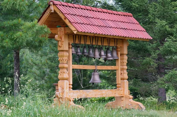 Escultura de madera con campanas y techo rojo, sobre el fondo del bosque . — Foto de Stock