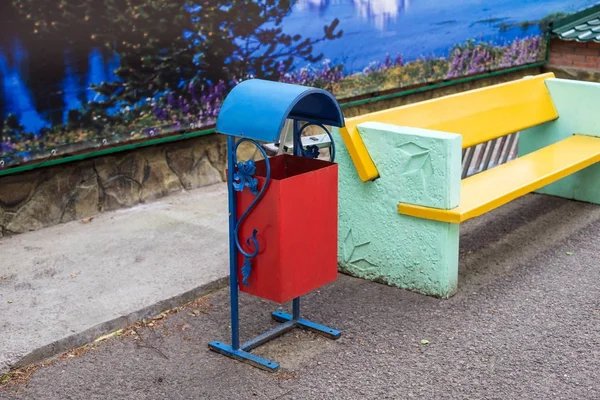 Кованый мусорный бак стоит рядом со скамейкой, на тротуаре . — стоковое фото