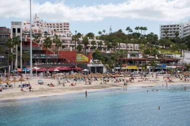 İnsanlar içinde belgili tanımlık geçmiş binaların sahildeki güneşlenme.