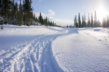 Snowdrifts ve batan güneşin arasındaki bir kayak yol ile kış manzarası.