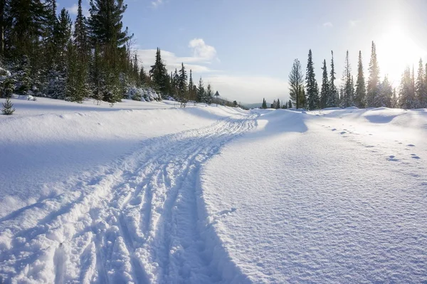 Snowdrifts ve batan güneşin arasındaki bir kayak yol ile kış manzarası.