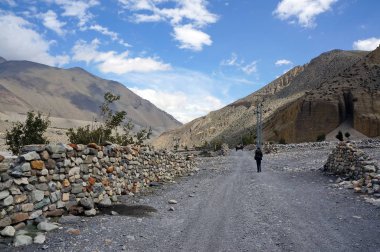 Turistler Himalayalar 'daki taş çitler boyunca toprak bir yol boyunca yürürler, Nepal' deki Yukarı Mustang 'e doğru..