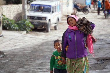 Jomsom, Mustang / Nepal - 21 Ağustos 2014: Kimliği belirsiz bir kadın, Nepal Mustang Bölgesi 'nde Jomsoma Caddesi boyunca bir çanta taşıyor ve bir çocuğa yol gösteriyor.
