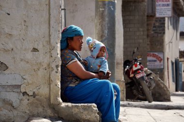 Jomsom, Mustang / Nepal - 21 Ağustos 2014: Kimliği belirsiz bir Nepalli kadın ve dizlerinin üzerinde küçük bir çocuk, bir şehir caddesinde bir evin duvarında oturuyor..