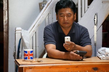 Jomsom, Mustang / Nepal - 21 Ağustos 2014: Kimliği belirsiz bir adam merdivenlerin arka planındaki cep telefonuna dikkatle bakıyor.