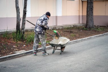 Yeniseisk, Krasnoyarsk Bölgesi / Rf - 13 Ekim 2019: Kapıcı kaldırımı süpürüyor ve çöpü sonbaharda binanın yakınındaki bir arabaya koyuyor.