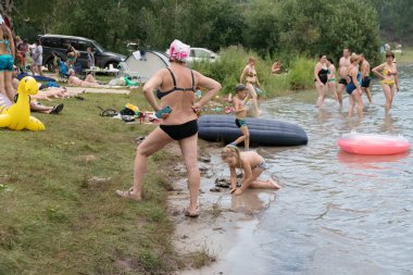 Round Lake, Krasnoyarsk Bölgesi / Rf - 3 Ağustos 2019: Bir kız bir yaz günü tatilcisinin arka planına karşı bir kadının nezareti altında gölün suyunda oynuyor.