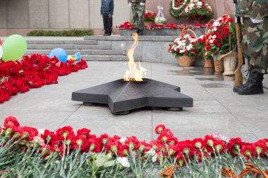 The eternal flame in the shape of a star burns in memory of those killed in the Second World War among fresh clove flowers. clipart