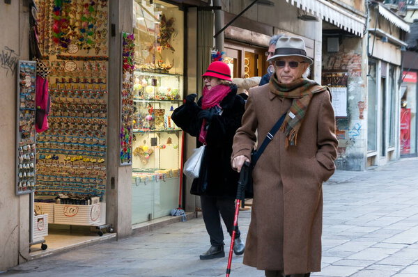 Венеция / Италия - 24 января 2019 года: пенсионер с палочкой ходит по старой узкой улице мимо витрин магазинов.