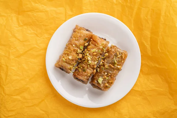 Traditional greek pastry saragli in a white plate on a yellow paper background — Stock Photo, Image