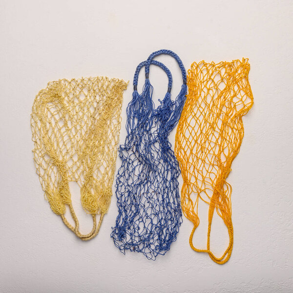 Concept of the three colored string bags made from natural materials on a light background. Environmental protection