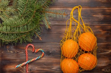 Ahşap arka planda ızgara şeklinde portakallar. Köknar dalları ve karamel kamışların yanında. Noel konseri