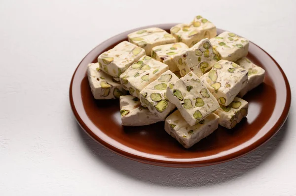 Восточная арабская нуга сладость с фисташками на коричневой керамической пластине на светлом фоне — стоковое фото