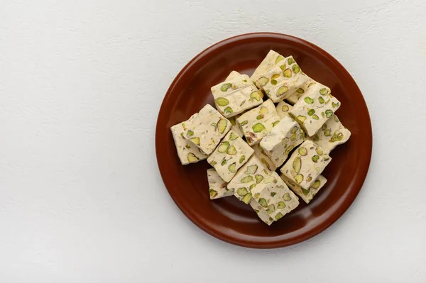 Eastern Arabic nougat sweetness with pistachios on a brown ceramic plate on a light background. Top view — Stock Photo, Image