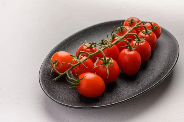 Red tomatoes on a green branch on a dark platter on a wooden background. Rustic style. Top view — Stock Photo, Image