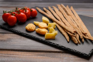 Çavdar ekmeği grissini, kiraz domatesleri, peynir ve yeşillikler, ahşap arka planda siyah dökme demir bir tahta üzerinde. Kırsal biçim