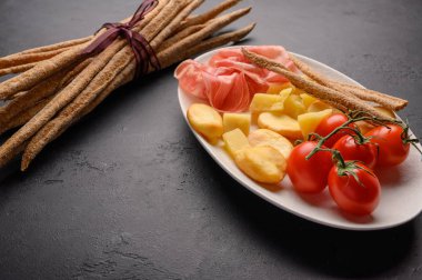 Geleneksel İtalyan yemekleri jambonlu Grissini ekmeği, peynirli domatesler ve siyah arka planda bir tabakta otlar. Sağlıklı stil. Boşluğu kopyala