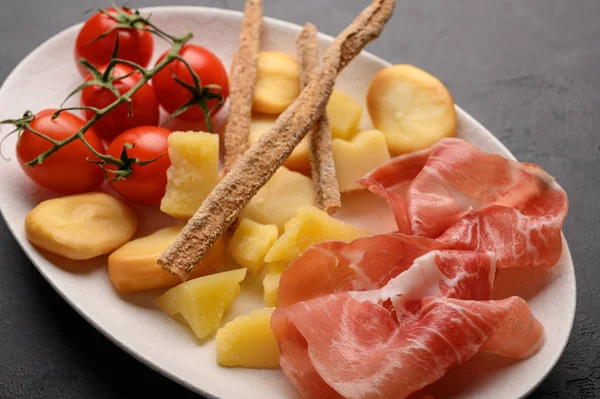 Italian food is grissini bread with prosciutto, cheese and tomatoes with herbs on a plate on a dark background. Healthy style. Close up — Stock Photo, Image